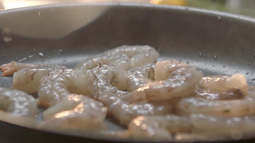 Shrimp is flipped and cooked in oil on a pan