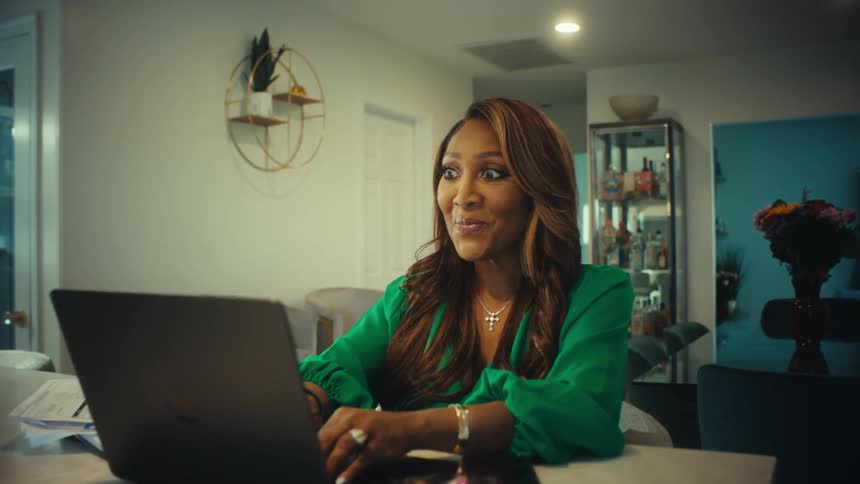 A business woman working on her laptop from home gets a look of surprise and then celebrates good news with a happy dance