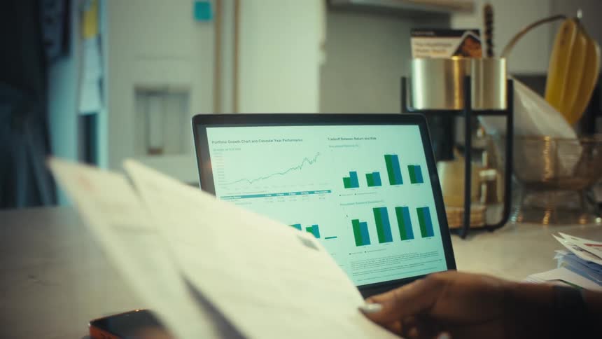 A person reviews their financial portfolio and sorts through paperwork while working from home at the kitchen counter