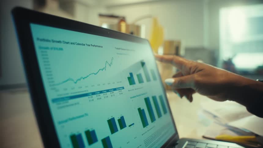 Slow motion close up of a woman's hands analyzing portfolio growth charts on a laptop in a bright home office