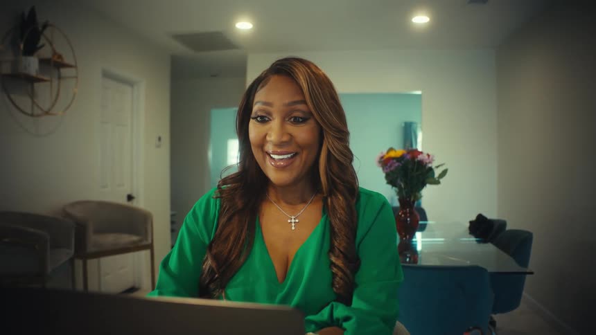 An elegant businesswoman working from home smiles with excitement and joy at what she sees on her laptop screen