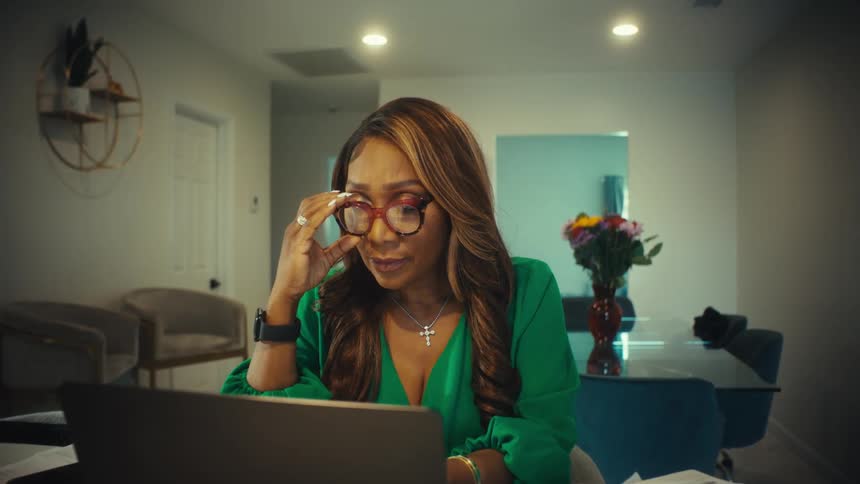 An elegant woman working from home takes off her glasses in happy surprise at what she sees on her laptop screen