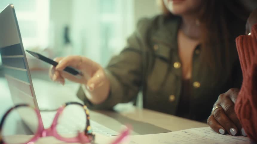 A close-up shot of two female colleagues collaborating and pointing at a laptop screen during a business meeting