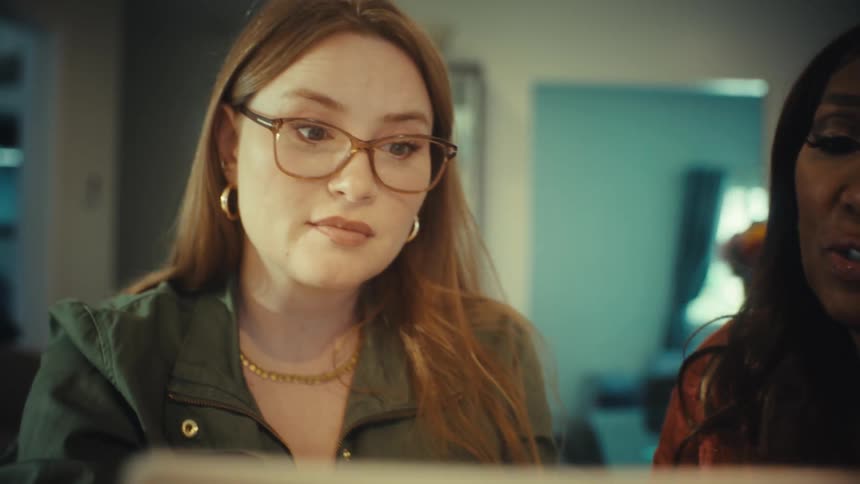 An experienced woman mentors her younger colleague as they collaborate on a project using a laptop in a modern office