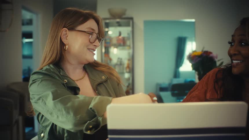 Two diverse businesswomen shake hands after a successful meeting while collaborating on a laptop in a modern home