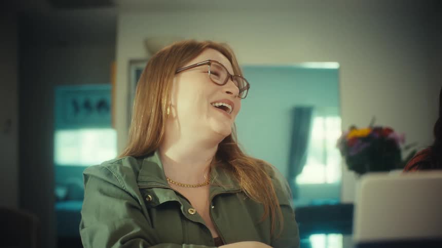Two diverse female friends laugh hysterically during a video call on their laptop in a modern home