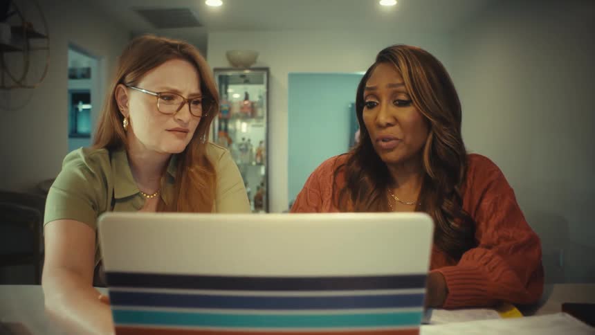 A slow push-in shot shows two diverse female friends reacting with shock and disgust to something on their laptop screen while working from home