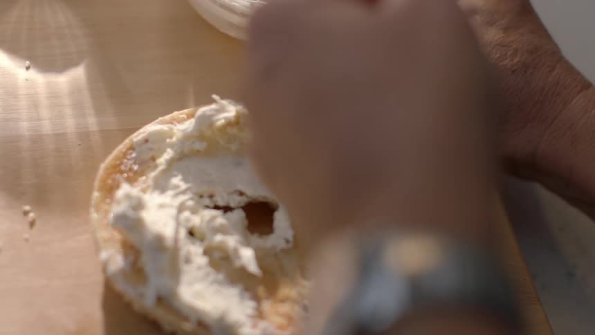 A person is spreading cream cheese on a bagel slice