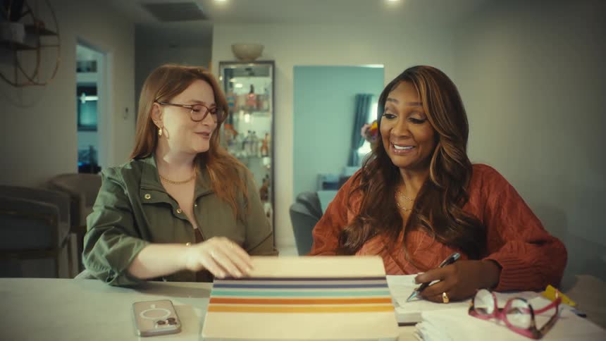 Two diverse businesswomen happily collaborate on a project from a home office, closing the laptop and shaking hands in agreement