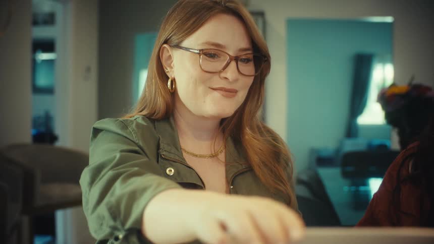 Close up of a smiling redhead professional explaining her work on a computer, then happily shaking hands with her partner in agreement