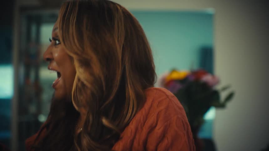 A middle-aged African American woman bursts into joyful, contagious laughter while sitting at a table in slow motion