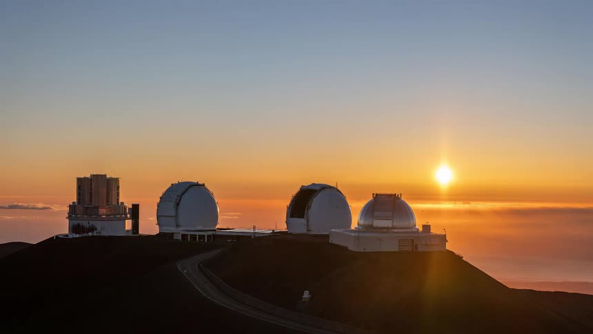 A stunning timelapse shows the sun setting behind the astronomical observatories on a mountain peak, painting the sky with brilliant orange hues