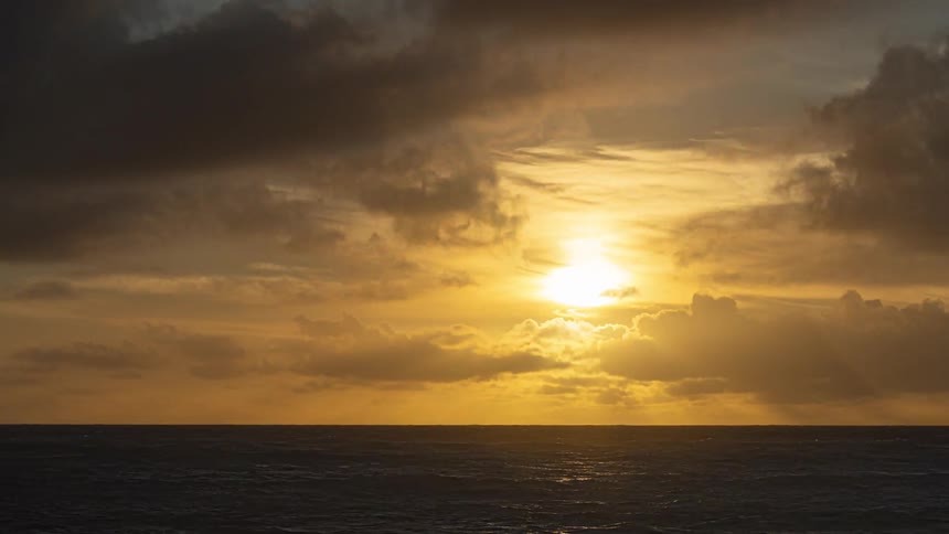 A breathtaking timelapse captures dark, stormy clouds parting to reveal a glorious golden sunrise over the rolling ocean waves