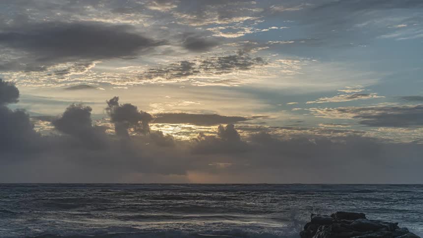 A dramatic time-lapse captures the sun breaking through dark, stormy clouds during a beautiful sunrise over the ocean