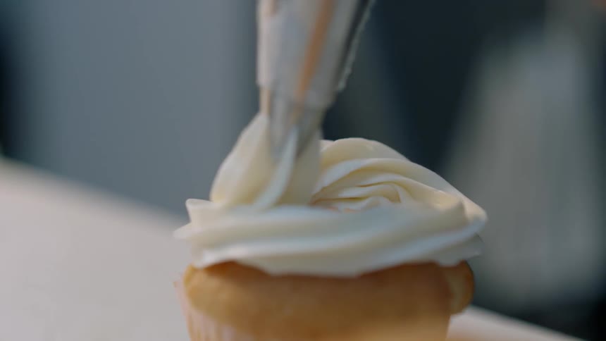 Someone putting frosting on a cupcake
