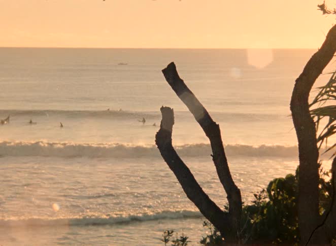 A scenic long shot of surfers waiting for waves on the ocean during a beautiful golden hour sunrise