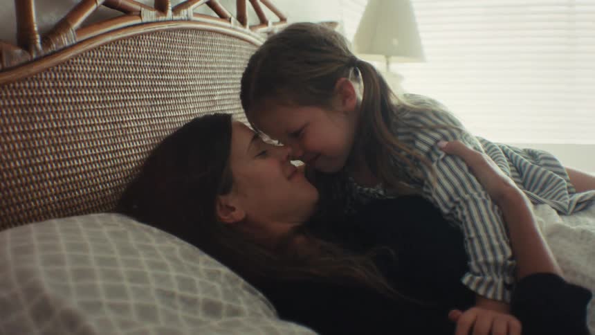 An affectionate mother and daughter share a loving moment as they cuddle in bed, rubbing noses and smiling