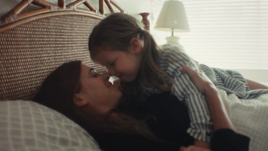 An affectionate mother and daughter share a loving moment as they cuddle in bed, rubbing noses and smiling