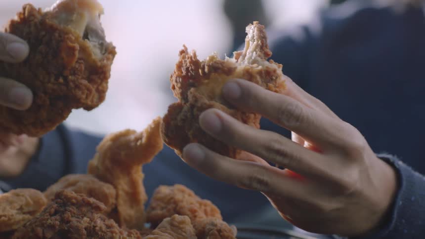 A person picks up a piece of chicken and begins eating