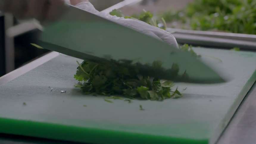 A restaurant employee dices fresh herbs on a cutting board
