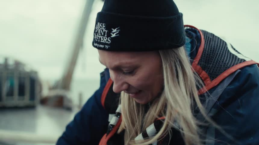 A content female deckhand smiles as she works on a commercial fishing vessel