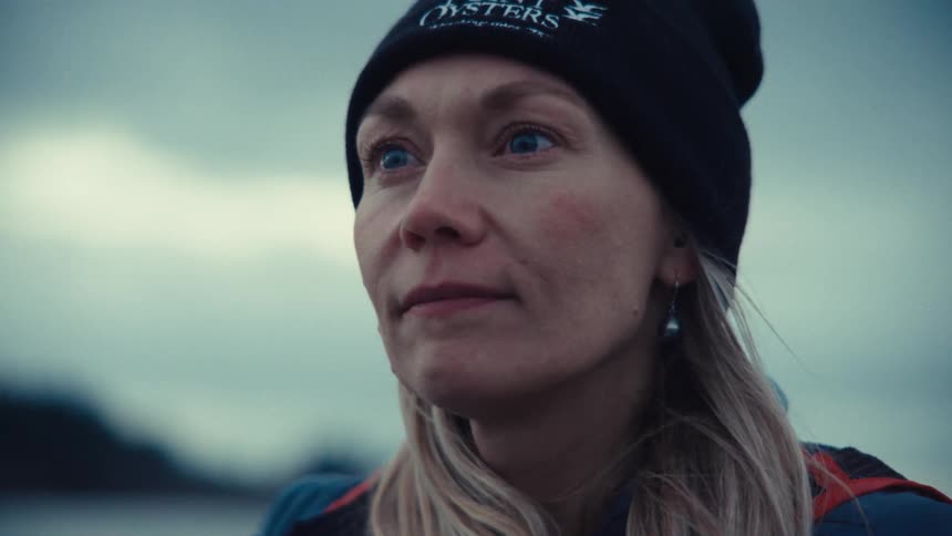 A close-up of a thoughtful woman in a black beanie looking out at the overcast sky with a pensive expression