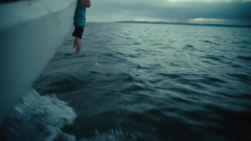 Cinemagraph loop of a hand trailing above the choppy water from a moving boat on a moody, overcast day