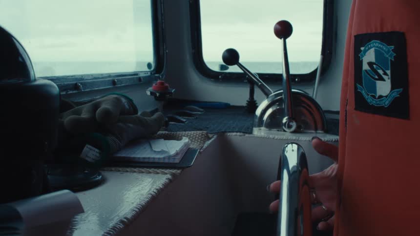 A person's hand operates the throttle inside a boat's wheelhouse with a view of the open sea