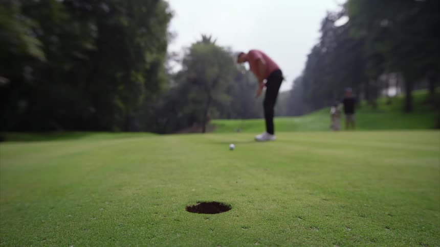 A golfer makes a successful putt as the golf ball rolls across the green and drops into the hole in one continuous shot