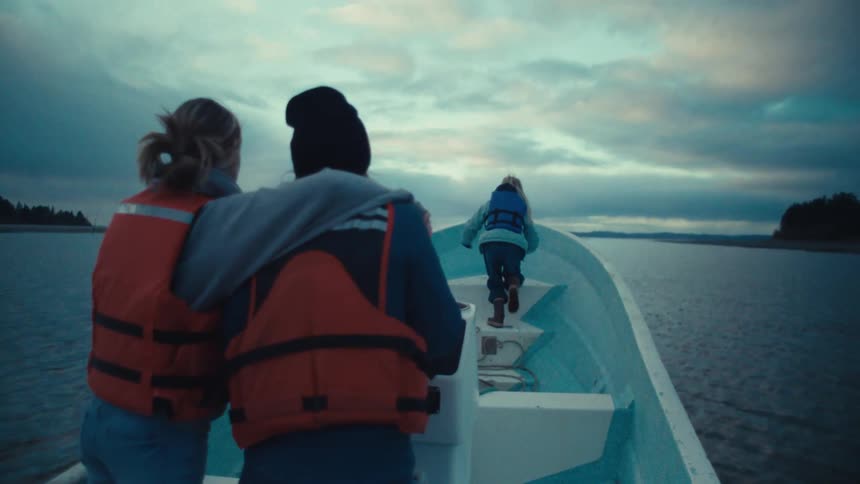 A family of three enjoys a serene boat ride across the water as their young daughter looks out from the bow at dusk