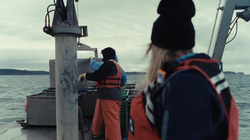 Fishermen work on the stern of a commercial boat on a cloudy day out on the water