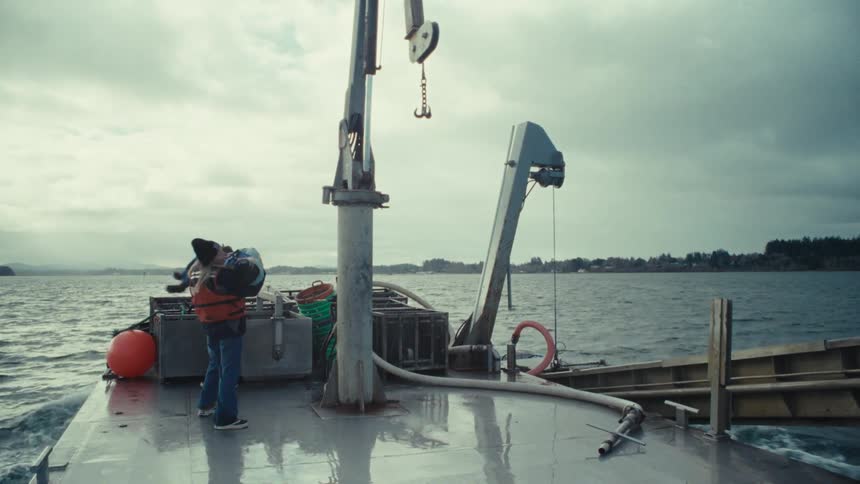 A parent in a life vest tenderly holds their child on the deck of a boat crossing the water in slow motion