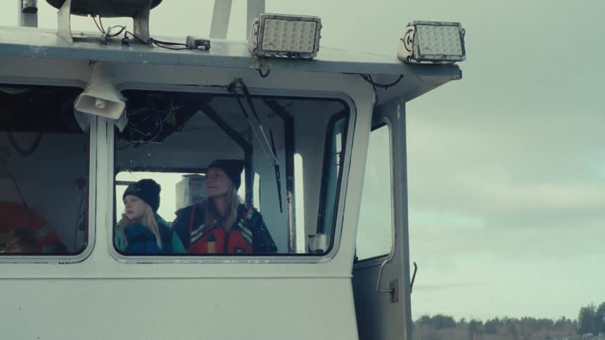 A female captain steers a boat with her family through calm waters on an overcast day