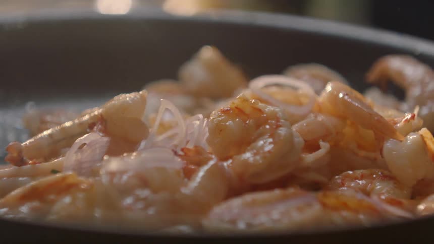 Onion slices are added to a skillet of cooking shrimp