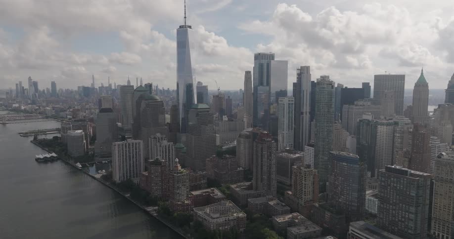 An aerial view of the Lower Manhattan skyline in New York City slowly pushes in from over the Hudson River on a partly cloudy day