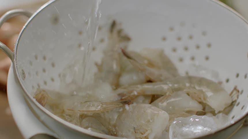 Water pouring over raw shrimp in strainer bowl