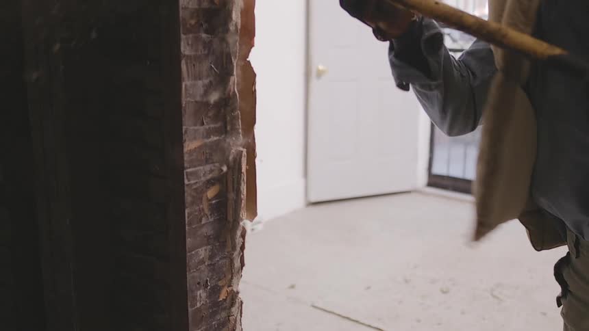 A senior woman in work boots happily demolishes an old wall with a crowbar in slow motion during a home renovation