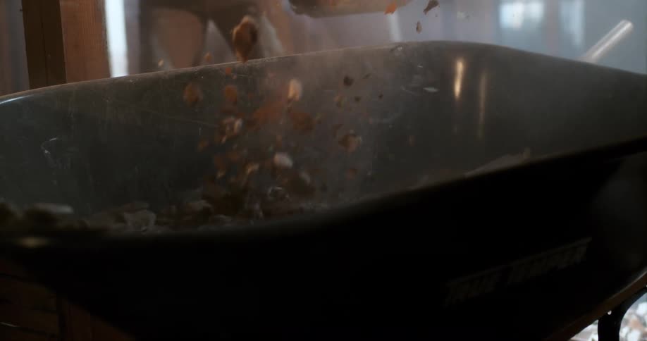 Dusty construction debris falls in slow motion from a shovel into a wheelbarrow at a worksite
