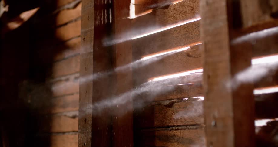 An explosion of dust and small particles blows through the cracks of a wooden wall in dramatic slow motion