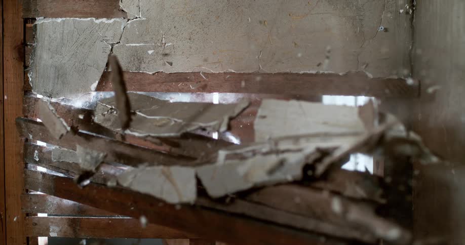 A sledgehammer smashes through a plaster and lath wall in extreme slow motion during a home demolition