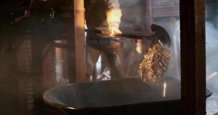 A construction worker wearing a respirator mask shovels demolition debris into a wheelbarrow in a dusty attic in slow motion