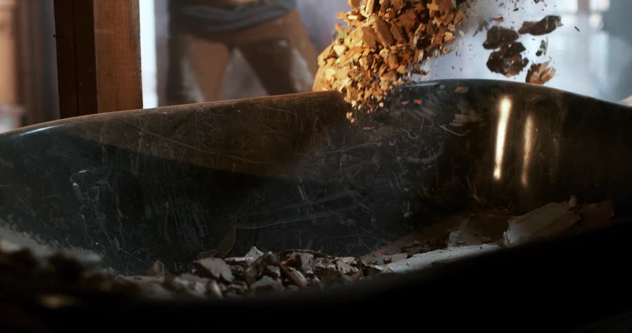 A construction worker dumps demolition debris from a shovel into a wheelbarrow in dramatic slow motion