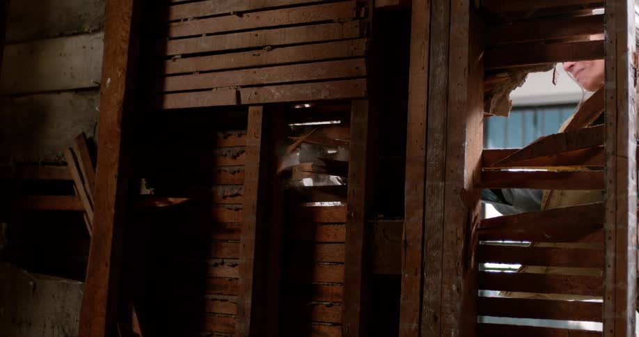 A person demolishes an old lath and plaster wall, with dust and wood debris flying in dramatic slow motion