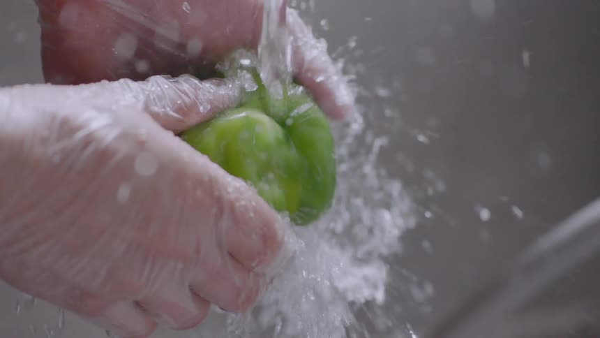 Person washing green pepper in sink
