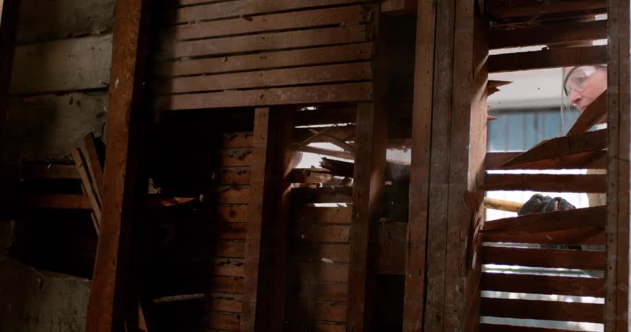 Slow motion view from inside a wall as a woman with a sledgehammer demolishes old lath and plaster