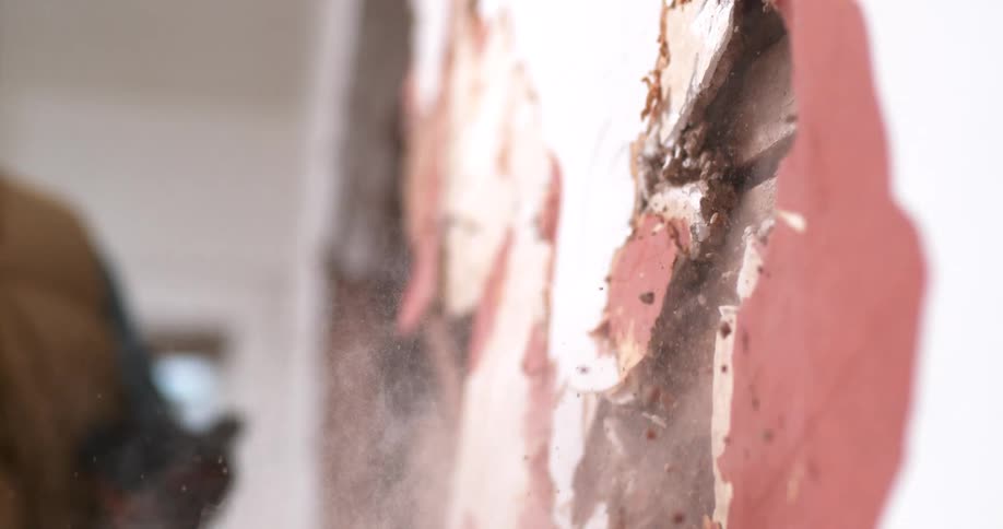 Extreme slow-motion footage shows a pickaxe smashing into a wall, sending dust and debris flying