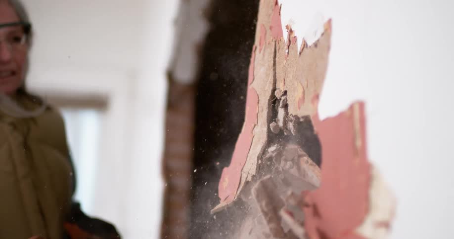 Extreme slow motion close up of a woman demolishing an interior wall with a large hammer, sending plaster and dust flying into the air