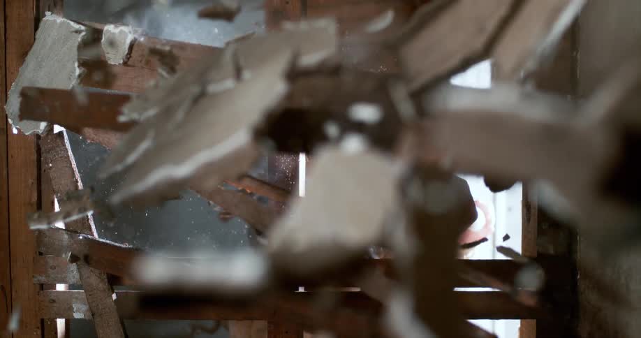 A worker smashes through a plaster and lath wall with a sledgehammer in extreme slow motion, sending debris flying