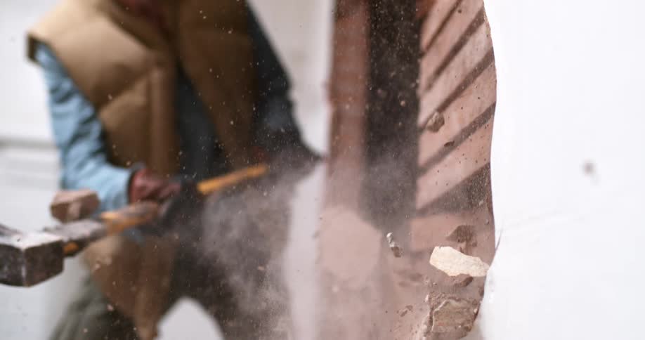 A close-up view in super slow motion of a sledgehammer smashing through a plaster and lath wall, sending dust and debris flying