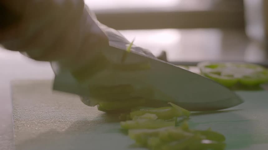 A restaurant employee dices peppers on a cutting board